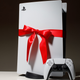 A PlayStation 5 controller is placed on a table in front of a PlayStatoin 5 console that is wrapped in a red bow. PlayStation 5 a